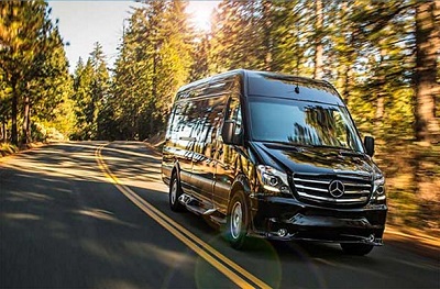 A lifestyle picture of the 2023 Midwest Automotive Designs G Series Mercedes-Benz Type B motorhome driving down a road lined with trees.