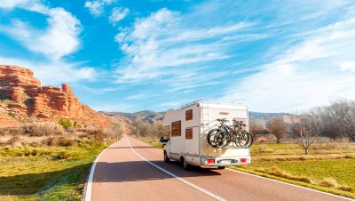A picture of an RV with bicycles on the back traveling down the open road towards a desert scene under a blue sky