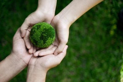A picture of two sets of hands holding a small, green, verdant Earth in their outstretched palms