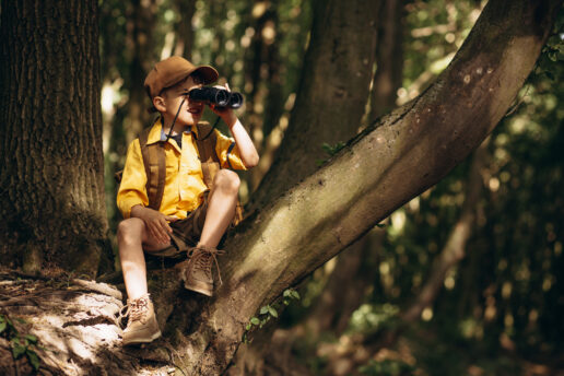 A picture of a Young boy in the woods with binoculars