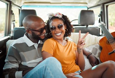 A picture of a black couple sitting together smiling next to a guitar in back of a Type B motorhome at the Coachella music festival