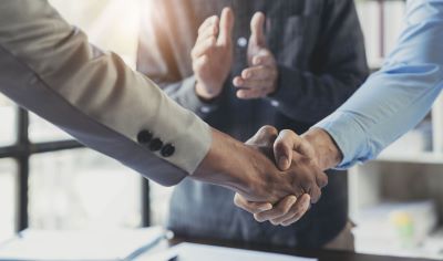 A picture of two people shaking hands with a third person clapping in the background