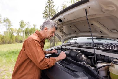 A picture of an older gentleman in a long-sleeved shirt looking into the engine compartment of an RV as he is parked on the side of the road