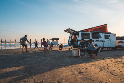 A picture of the TAXA Mantis travel trailer with a young family playing games at the beach