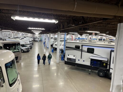 A picture of an interior of a Camping World showroom in Wisconsin with three people walking down the center of a large aisle between RVs
