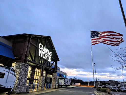 A picture of a Camping World storefront in Wisconsin with the American flag blowing in the breeze in front of it at dusk