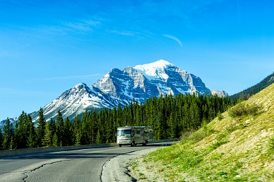 A picture of an RV rolling on the road in Banff National Park Canada with a view of mountains and clear sky in the background