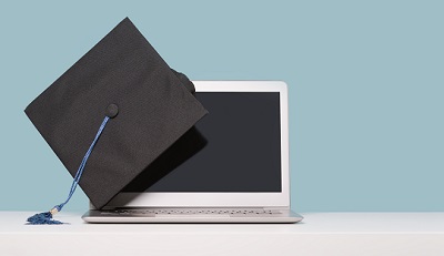 A picture of a mortar board hanging on the corner of a laptop, a metaphor for online university