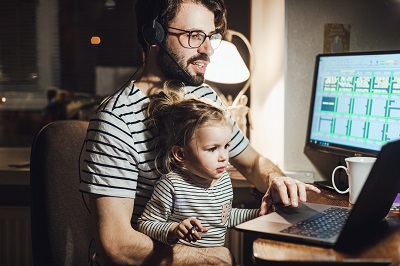 A picture of a Millenial father posting on the computer with his child on his lap