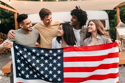 A picture of happy young people from various ethnic backgrounds holding a flag in front of an RV campsite