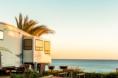 A picture of an RV by the ocean with a palm tree in the background