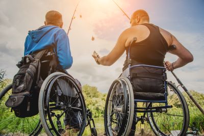 A picture of two men in wheelchairs fishing their backs are turned toward the camera and they are facing the sun