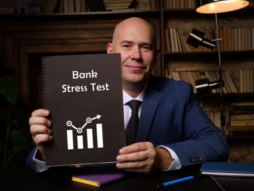 A picture of a man in a professional office holding up a book that says Bank Stress Test on the cover.