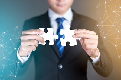 A picture of a man in a suit putting two complementary puzzle pieces together symbolizing a merger