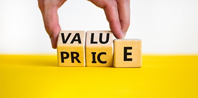 A picture of a hand turning over wooden "PRICE" Blocks on a yellow platform to spell the word "VALUE"