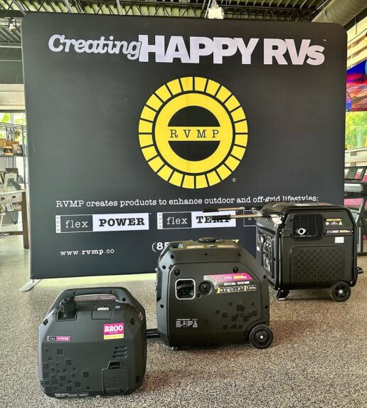 A picture of three RVMP generators on the floor with a sign behind them that reads "Creating Happy RVs" and the company logo in the middle of the sign.