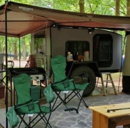 A picture of the exterior of the 2024 Radical Trailer overland trailer with the awning out and campsite set up.