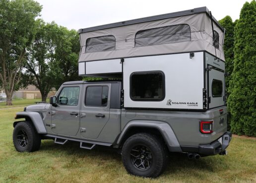 A picture of a Soaring Eagles Camper OV-X 5 atop a Jeep Gladiator, parked on a grass field.