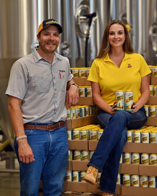 A picture of KOA CEO Toby O'Rourke sitting on a stack of beer with Meadowlands Brewing owner Travis Peterson standing next to her.