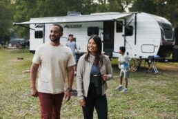 A picture of a couple walking in a grass area with their Winnebago Access travel trailer parked behind them.