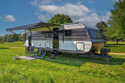 A picture of a Cruiser RV Avenir travel trailer set up in a field on a sunny day.