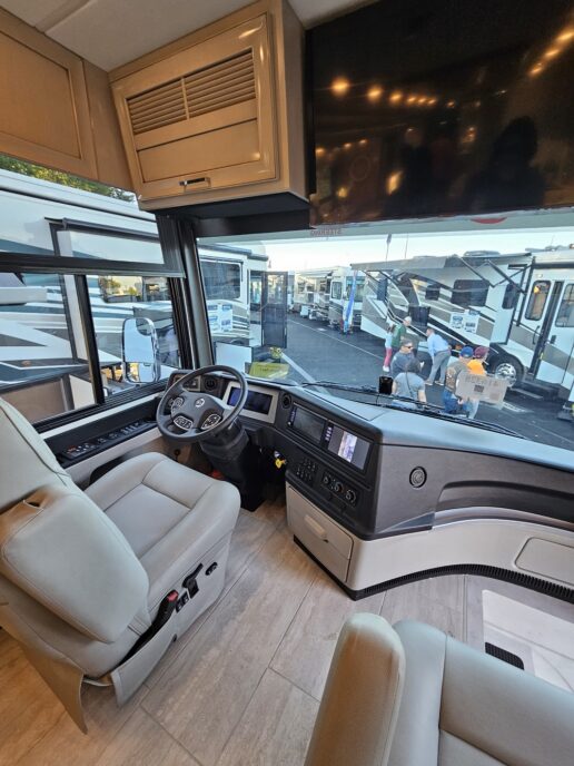 A picture from the 2023 America's Largest RV Show in Hershey, Pennsylvania, looking through a motorhome's front windshield to numerous motorhomes parked on the lot.