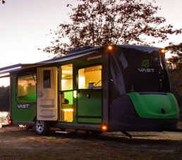 A picture of the SylvanSport Vast exterior parked near a tree with its interior lights on as sunset falls.
