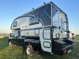 An exterior side picture of the nuCamp Cirrus 920 truck camper sitting atop a truck parked on the grass.