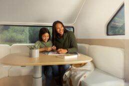 A picture of a woman and young girl sitting on the dinette in the front of a Pebble Flow electric travel trailer.