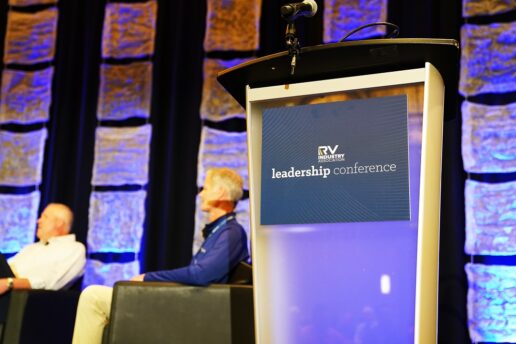 A picture of the podium at the 2023 RVIA Leadership Conference with Thor's Bob Martin and RVIA President Craig Kirby blurred on stage in the background.