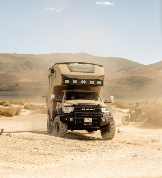 A lifestyle picture of a Storyteller Overland Hilt adventure truck driving through sand in a valley surrounded by mountains.