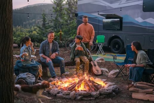 A photo of a family sitting around a fire next to their RV.
