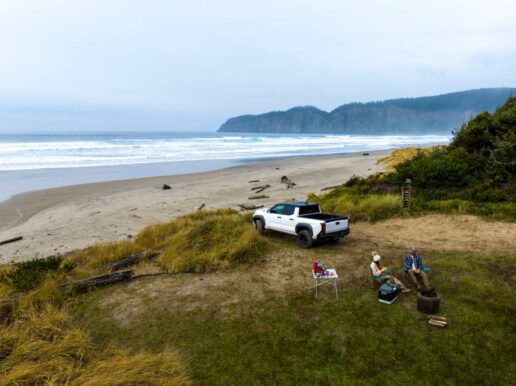 A photo of a truck parked just off the beach with a group of campers around a campsite.