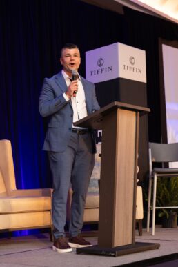 A picture of Leigh Tiffin speaking behind a podium during a presentation at Tiffin Motorhomes' 2025 dealer meeting in Nashville, Tennessee.